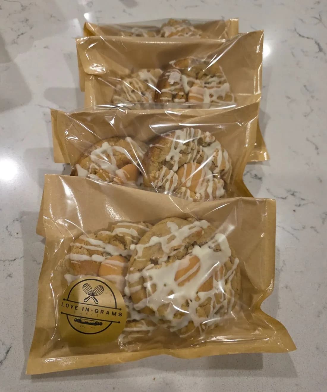Large iced cookies packed in clear-front kraft bags, the nearest closed with a gold Love In-Grams sticker
