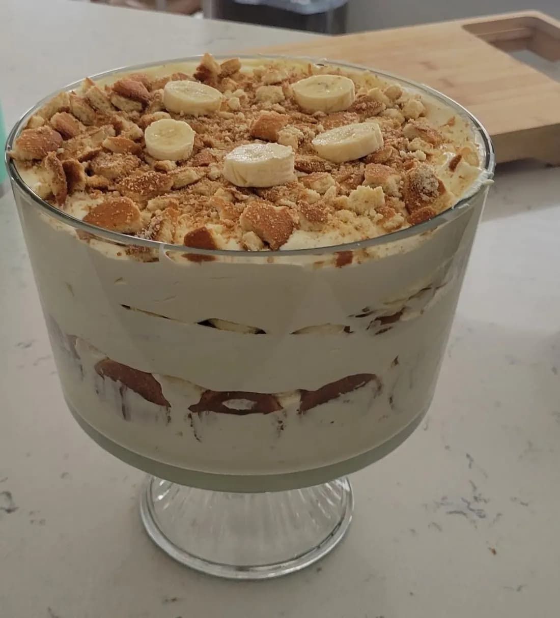 A layered pudding trifle in a footed glass bowl, topped with banana slices and cookie pieces